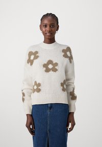 Maglione crema con motivi floreali marroni, colletto e polsini a costine, e una vestibilità comoda. Abbinato a una gonna in denim con uno spacco frontale.