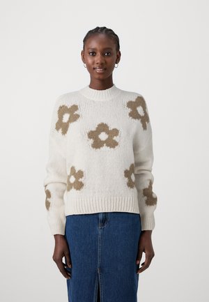 Maglione crema con motivi floreali marroni, colletto e polsini a costine, e una vestibilità comoda. Abbinato a una gonna in denim con uno spacco frontale.