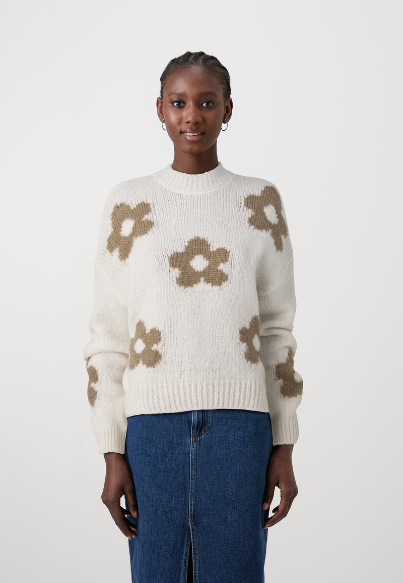 Maglione crema con motivi floreali marroni, colletto e polsini a costine, e una vestibilità comoda. Abbinato a una gonna in denim con uno spacco frontale.