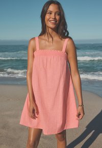 Rosa ärmlös klänning med rynkad överdel och avslappnad passform. Tillverkad av lätt tyg, med en enkel design och når till mitten av låret.
