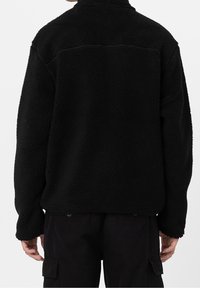 Zwarte fleece pullover met een gestructureerd oppervlak, hoge kraag en een eenvoudig achterkantnaadontwerp. Ruimvallend met lange mouwen.