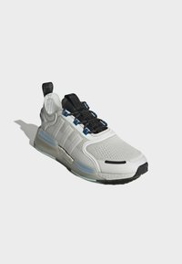 Vit sportskor med texturerad ovandel, svarta snören och blå accenter. Utrustad med en vadderad sula och logodetaljer på sidan.