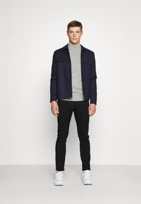 Navy shirt jacket, gray turtleneck, black pants, and white sneakers. The jacket features side pockets and a button closure.