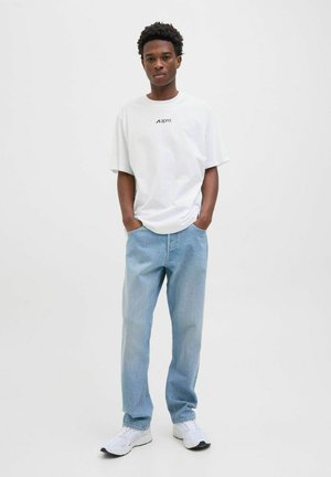 Hvid oversized t-shirt med sort logo, parret med lysevaske lige bukser og hvide sneaks med sorte såler.