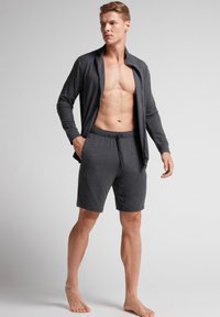 Grå zip-up jacka över en figursydd kropp, parat med shorts med elastisk midja. Båda plaggen har en mjuk textur och en avslappnad design.