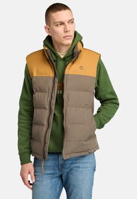 Padded vest in brown with a tan upper section. Features a zip closure, two side pockets, and ribbed texture on the upper.