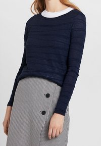 Granatowa bluzka z długim rękawem w poziome teksturowane paski, w połączeniu z czarno-białą spódnicą w kratę z dużymi guzikami.