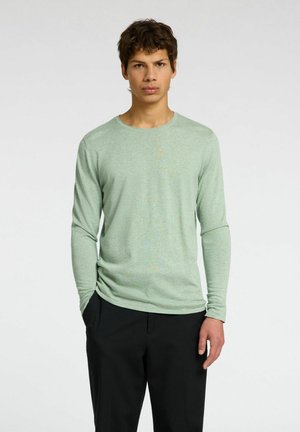 Lange mouwen, lichtgroene T-shirt gemaakt van zachte stof met een ronde halslijn en aansluitende mouwen, gedragen met zwarte broek.