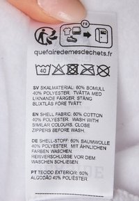 Etikett mit Pflegehinweisen und Materialzusammensetzung: 60 % Baumwolle, 40 % Polyester. Gedruckter Text in mehreren Sprachen. Weißer Hintergrund.