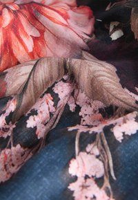 Tessuto floreale con grandi fiori rossi e rosa e delicati fiori rosa chiaro su uno sfondo blu scuro; texture morbida.