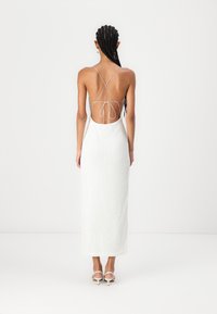 Λευκό, υφασμένο φόρεμα μέχρι τον αστράγαλο με χαμηλή πλάτη και σταυρωτές τιράντες, με εφαρμοστό σχήμα και λεπτή δέσιμο στο πίσω μέρος.