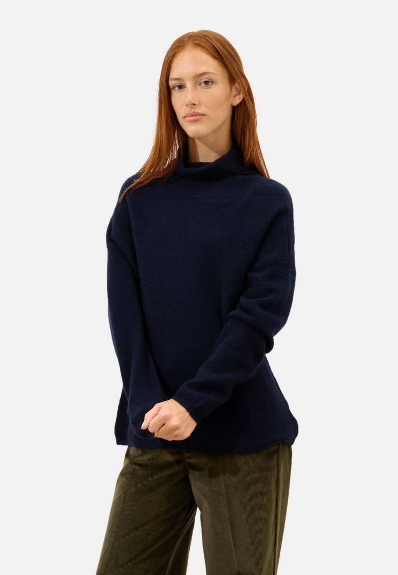 Marineblauer Rollkragenpullover mit langen Ärmeln und weicher Textur. Bietet eine lockere Passform und gerippte Abschlüsse, getragen über olivgrünen Hosen.