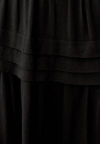 Abito nero con pieghe a strati, realizzato in tessuto leggero dalla texture liscia, che mostra un design semplice ed elegante.