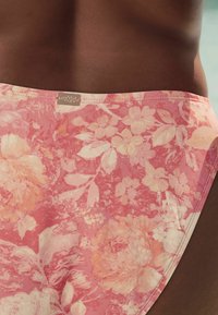 Cvetni kopalni spodnji del v odtenkih roza in breskev; ima teksturirano tkanino in majhno kovinsko oznako na pasu.