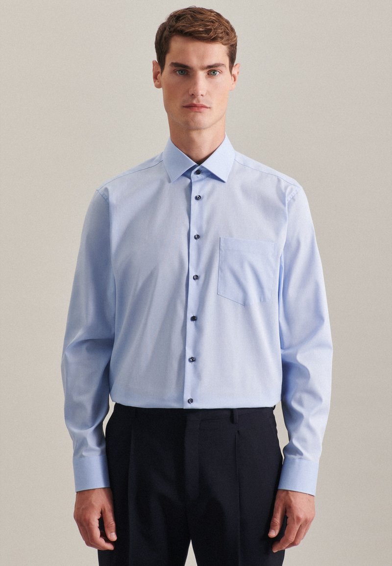Camicia azzurra a maniche lunghe con colletto a bottoni, tasca frontale e bottoni scuri; realizzata in tessuto morbido con una sottile texture.