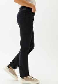 Schwarze, gerade Jeans aus Denim mit Gesäßtaschen, mittelhoher Taille und dezenten Nähten, kombiniert mit hellen Sneakers.