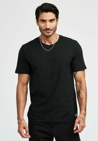 Svart t-shirt med kort ärm i bomullsmaterial och rundad halsringning. Har en liten triangulär logotyp vid den nedre fållen.