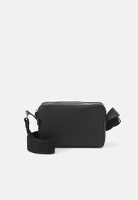 Sac crossbody rectangulaire noir avec fermeture éclair argentée et large bandoulière réglable, posé sur un fond blanc.