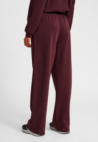 Bordeaux wijde broek van zacht materiaal met een elastische tailleband, voorzien van een subtiele logo aan de linkerkant en een gestructureerde afwerking.
