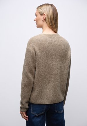 Beige Fleece-Pullover mit strukturiertem Oberflächen, Rundhalsausschnitt, langen Ärmeln und lockerer Passform, kombiniert mit blauen Jeans.