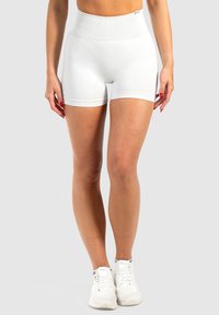 Witte hoge sportshorts met een geribbelde textuur en een elastische tailleband, gecombineerd met witte sportschoenen tegen een grijze achtergrond.