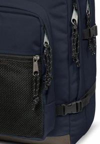 Námořnický batoh s strukturovanou černou síťovanou kapsou, dvojitými zipovými oddíly a pevným popruhem s nastavitelnými sponami pro bezpečné uzavření.