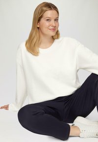 Witte longsleeve sweatshirt met een ronde halslijn, gecombineerd met donkere broek en witte sneakers. Zachte textuur, casual pasvorm, minimalistisch ontwerp.