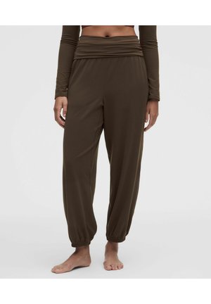 Femme portant un pantalon marron ample taille haute avec des chevilles froncées et un crop top assorti à manches longues, debout pieds nus sur un fond uni.