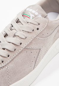 Hellgraue Sneakers aus Wildleder mit flachen Schnürsenkeln, gestanzten Details und einer weißen Gummisohle. Mit Logo auf der Zunge und mehrfarbigen Akzenten.