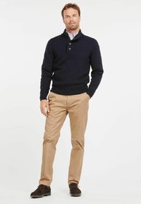 Marineblauer Strickpullover mit einem geknöpften Kragen, kombiniert mit hellbraunen Chinos. Das Outfit wird mit dunkelbraunen Wildlederschuhen abgerundet.