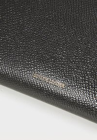Cuir véritable noir avec une surface texturée. Présente un motif en relief et un texte métallique indiquant "CUIR VÉRITABLE". Fini lisse et poli.
