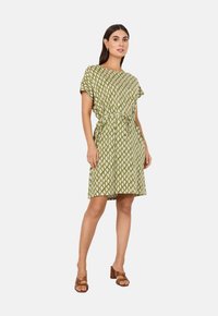 Grünes gemustertes Kleid mit kurzen Ärmeln, tailliertem Bund und lockerer Passform. Der Stoff hat ein Rautenmuster in Hellgrün und Creme.
