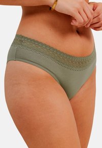 Culotte de bikini en mélange de coton vert olive avec une taille en dentelle scallopée décorative, présentant une texture lisse et des coutures minimales.