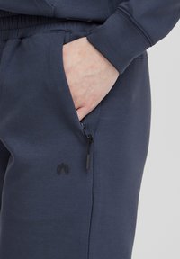Námožné jogger nohavice z mäkkej tkaniny, s elastickým pásom, bočnými vreckami a zipsom so čiernymi kovovými doplnkami.