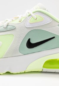 Zapatillas verdes y blancas con materiales de malla y ante, un logo de Nike negro y una unidad de amortiguación visible en la suela.