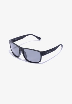 Mustad mustvalgudes mustad prillid hallide läätsedega, millel on tekstuuriga raam ja sirged käed. Kaubamärk "Hawkers" on trükitud küljele.