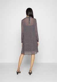 Schwarz-weißer, gemusterter Kleid mit langen Ärmeln, das einen Volant-Saum und einen Schlüsselloch-Rücken mit einer Bindeschließe aufweist. Glattes, leichtes Material.