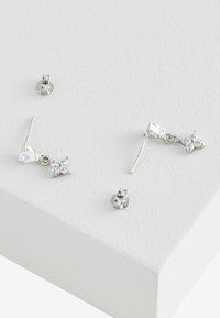 Orecchini a perno in argento con un design a farfalla, uno dei quali presenta un accento pendente in pietra, caratterizzati da gemme trasparenti e una finitura lucida.