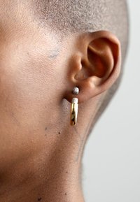 Gold hoop earring with a polished finish, paired with a small textured silver stud; worn on the earlobe against skin with a natural tone.
