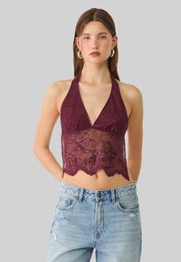 Burgundy lace halter-top dengan bordir bunga dan tepi berlekuk, dipadukan dengan celana jeans biru muda yang distressed, menciptakan tampilan berlapis.