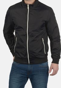 Černá bomber bunda s předním zipem, dvěma bočními kapsami, žebrovanými manžetami a lemem, bílými doplňky na zip a hladkým, lesklým povrchem.