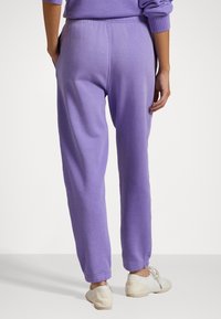 Lila sweatpants med elastisk midja, sidofickor och avsmalnande muddar. Mjukt tyg med en slät textur och jämn färg genom hela plagget.