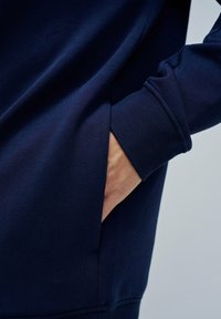 Sudadera azul marino con una textura suave, puños acanalados y un bolsillo lateral. Presenta un ajuste relajado y un diseño limpio y minimalista.