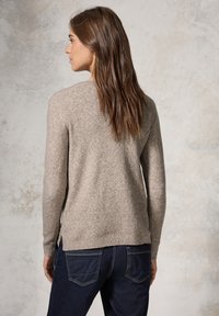 Pullover in maglia di colore marrone chiaro, con texture, maniche lunghe, scollo rotondo e spacchi laterali, abbinato a jeans in denim scuro.