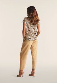 Top con estampado floral en beige y negro, con mangas cortas; combinado con pantalones sueltos de color marrón claro y sandalias de tacón alto transparentes.