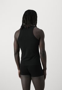 Black cotton tank top with a fitted design, featuring wide shoulder straps and a smooth texture, paired with matching black shorts.