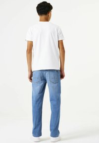 Camiseta blanca de manga corta combinada con unos pantalones vaqueros de mezclilla azul claro. Los vaqueros tienen bolsillos traseros con detalles de costura y son de corte recto.