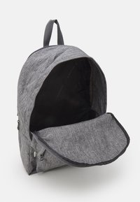 Gray fabric backpack with a textured exterior, a zippered main compartment, and a flap closure. Interior is black with branding details.