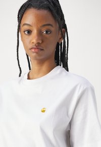 Witte katoenen t-shirt met een klein gouden golflogo op de linker borst. Zachte textuur en een eenvoudige ronde hals.