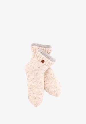 Gestrickte Socken in Cremefarbe mit einem strukturierten Muster, die einen flauschigen grauen Bund und ein kleines braunes Labelakzent aufweisen.